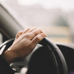 female driver with one hand on steering wheel